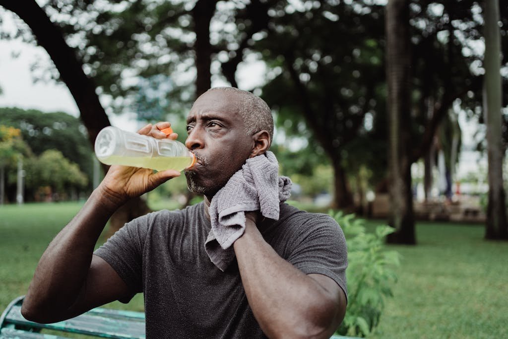 Adult man drinking sports beverage and wiping sweat in a park.