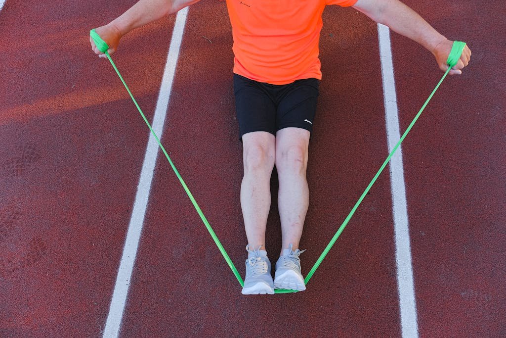 An adult male athlete working out with a green resistance band on a running track. Perfect for fitness and wellness themes.