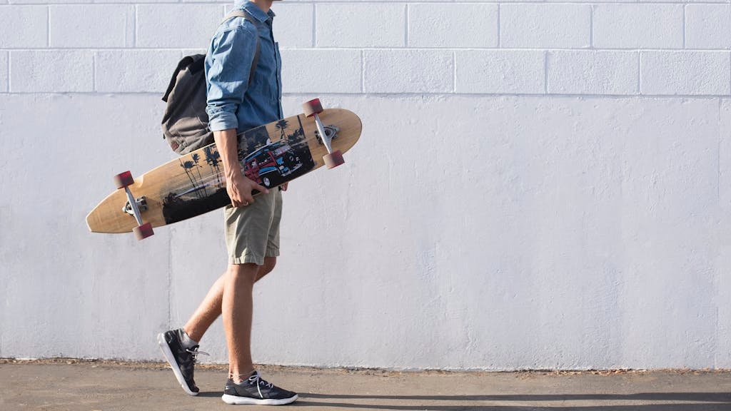 Casual young man walking with longboard against a white brick wall in Sanger, California.