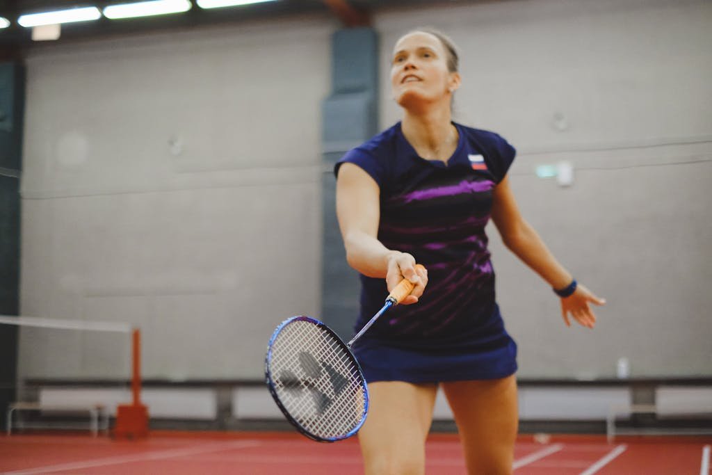 Focused female athlete playing badminton on an indoor court.