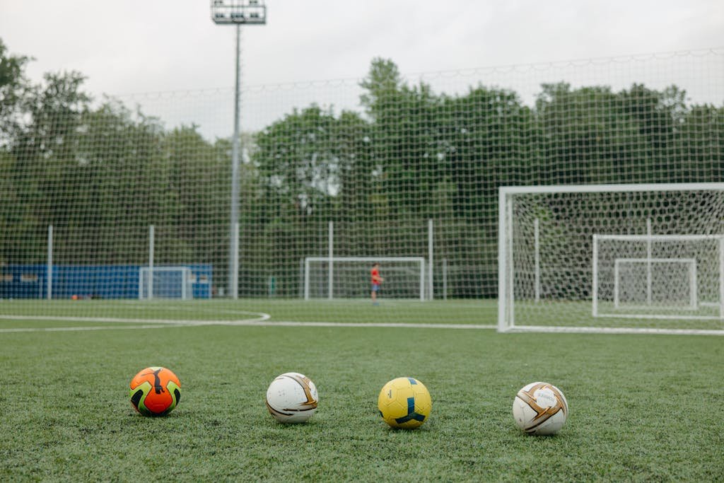 Four soccer balls on an outdoor field near goalposts, ideal for sports themes.