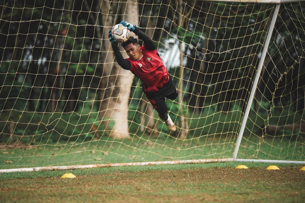 Soccer goalie making an impressive mid-air catch during a match on a green field.