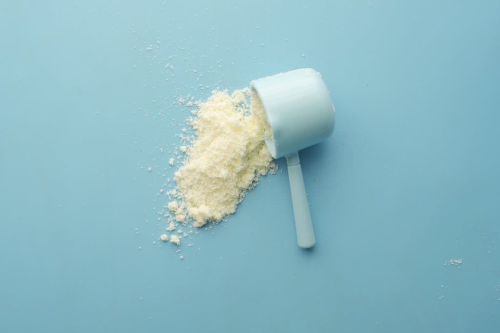 White powder spilled from a scoop on bright blue background. Clean and minimalistic food photo.