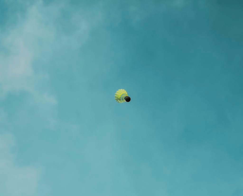 Yellow shuttlecock soaring against a clear blue sky. Minimalist sports image.