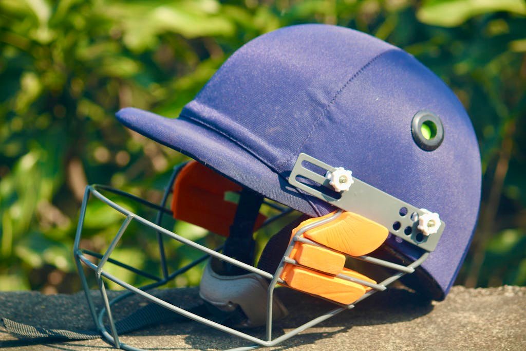 A blue cricket helmet placed outdoors with lush greenery in the background, showcasing sports equipment.