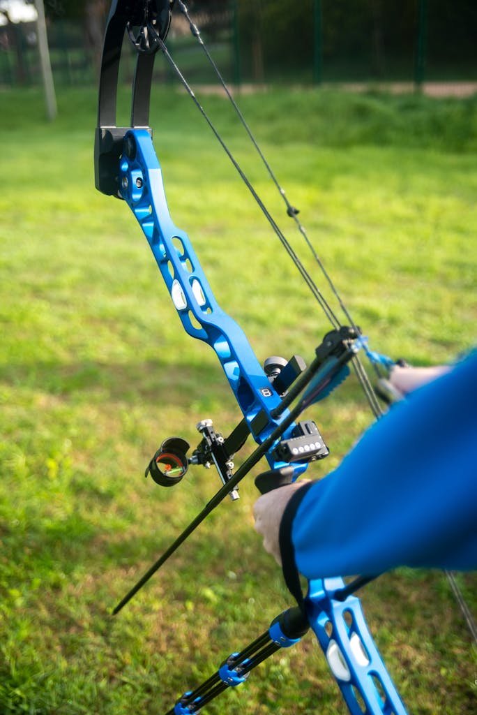 Close-up of a person holding a blue compound bow outdoors.