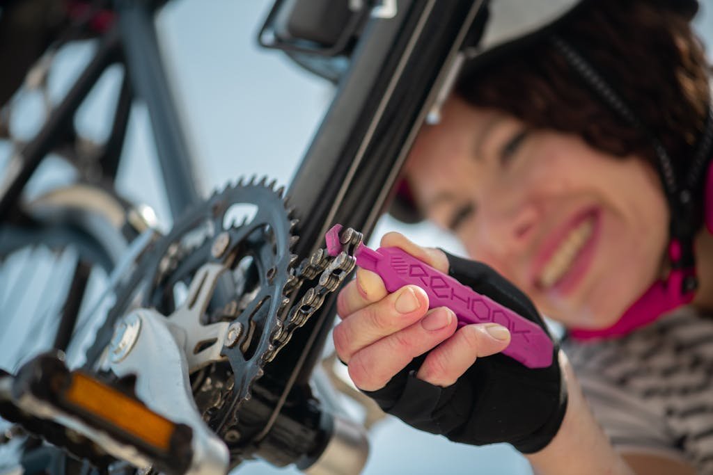 Close-up of a woman using a tool to repair a bicycle chain outside.