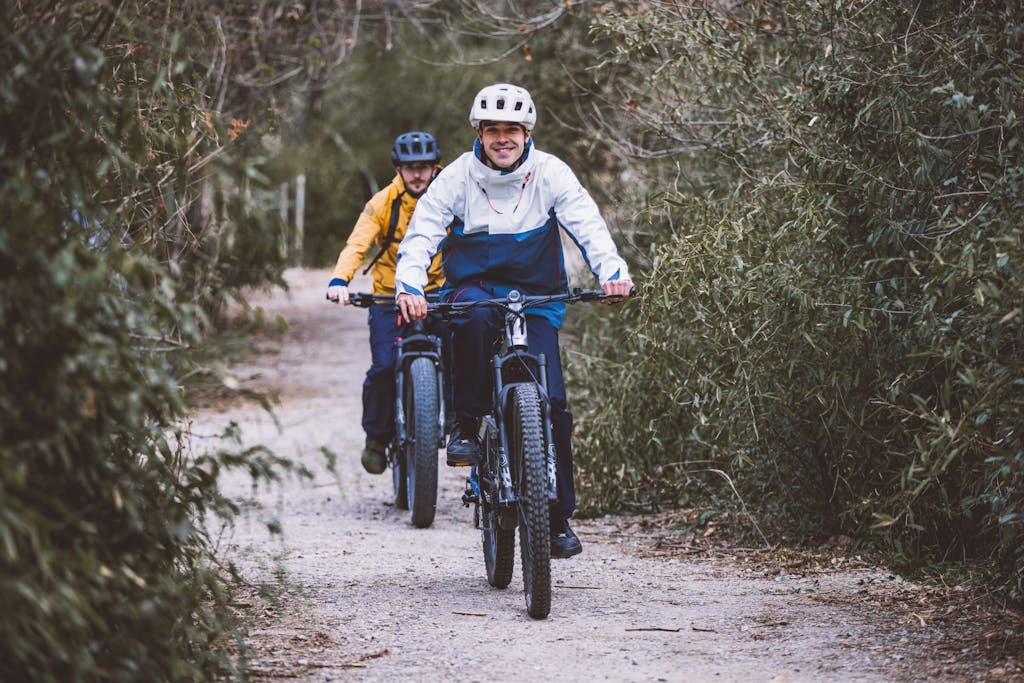 Two men ride bicycles along a forest path, enjoying a day of recreation outdoors.