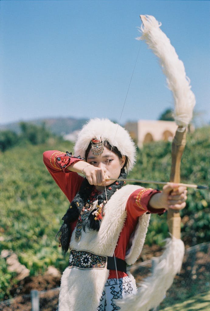 Woman in traditional attire practicing archery outdoors. Cultural heritage displayed.