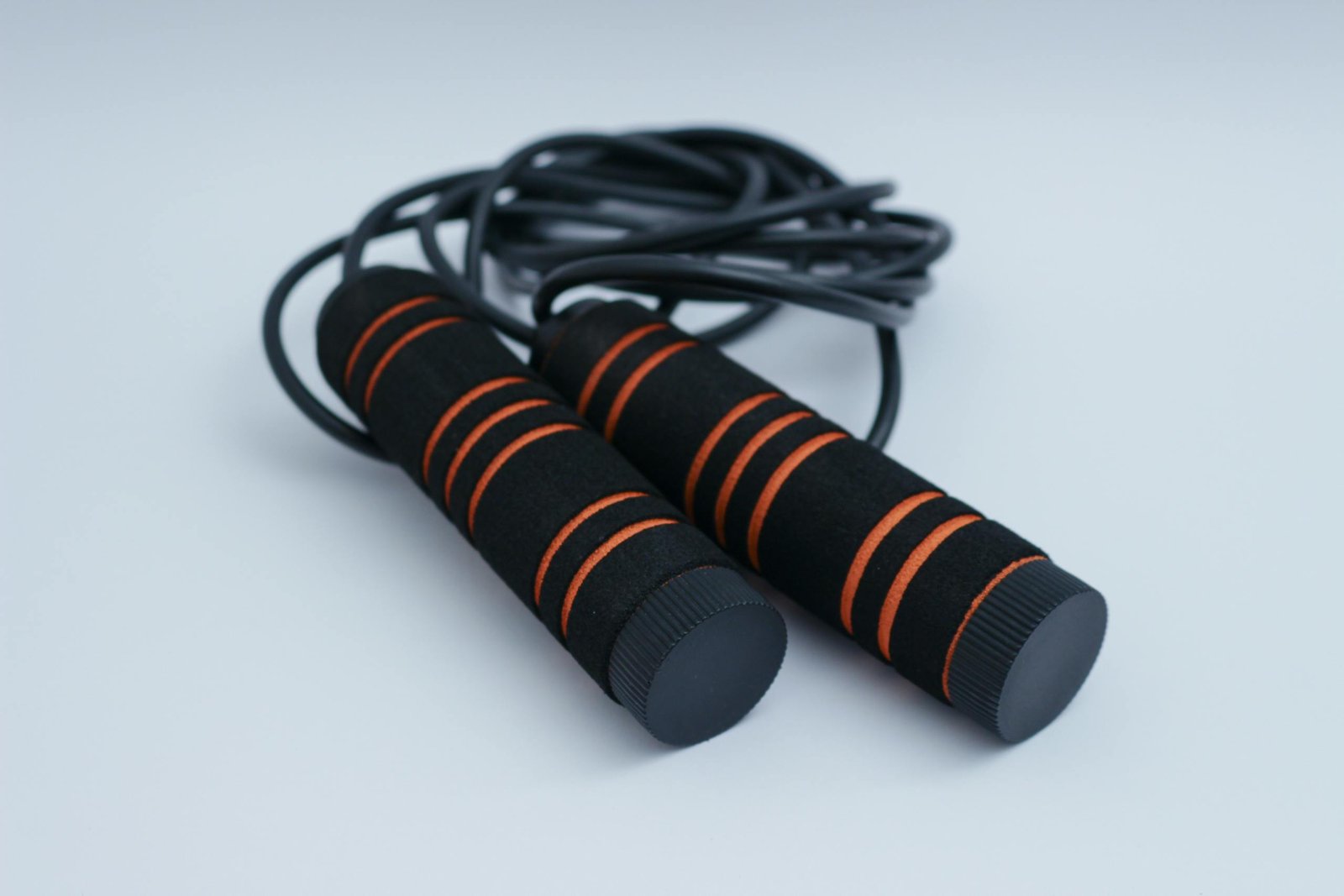 A minimalist close-up of black and orange exercise skipping rope on a clean white background.