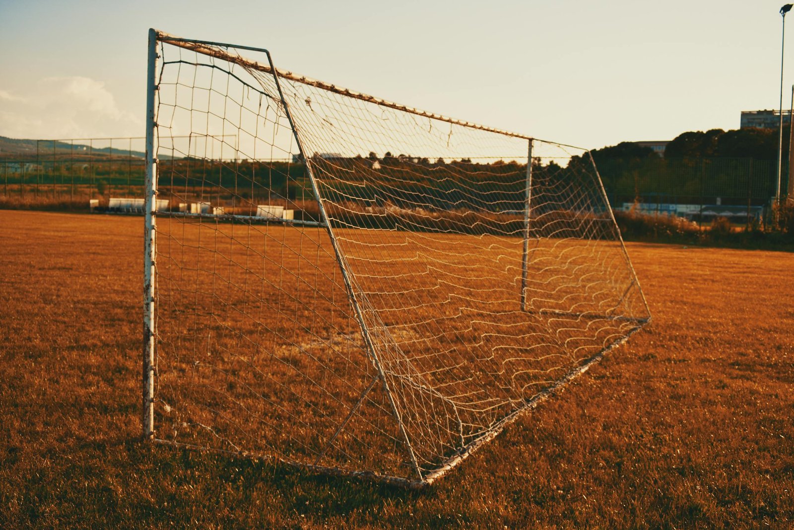 A quiet soccer field with a goalpost at sunset, reflecting a peaceful atmosphere.