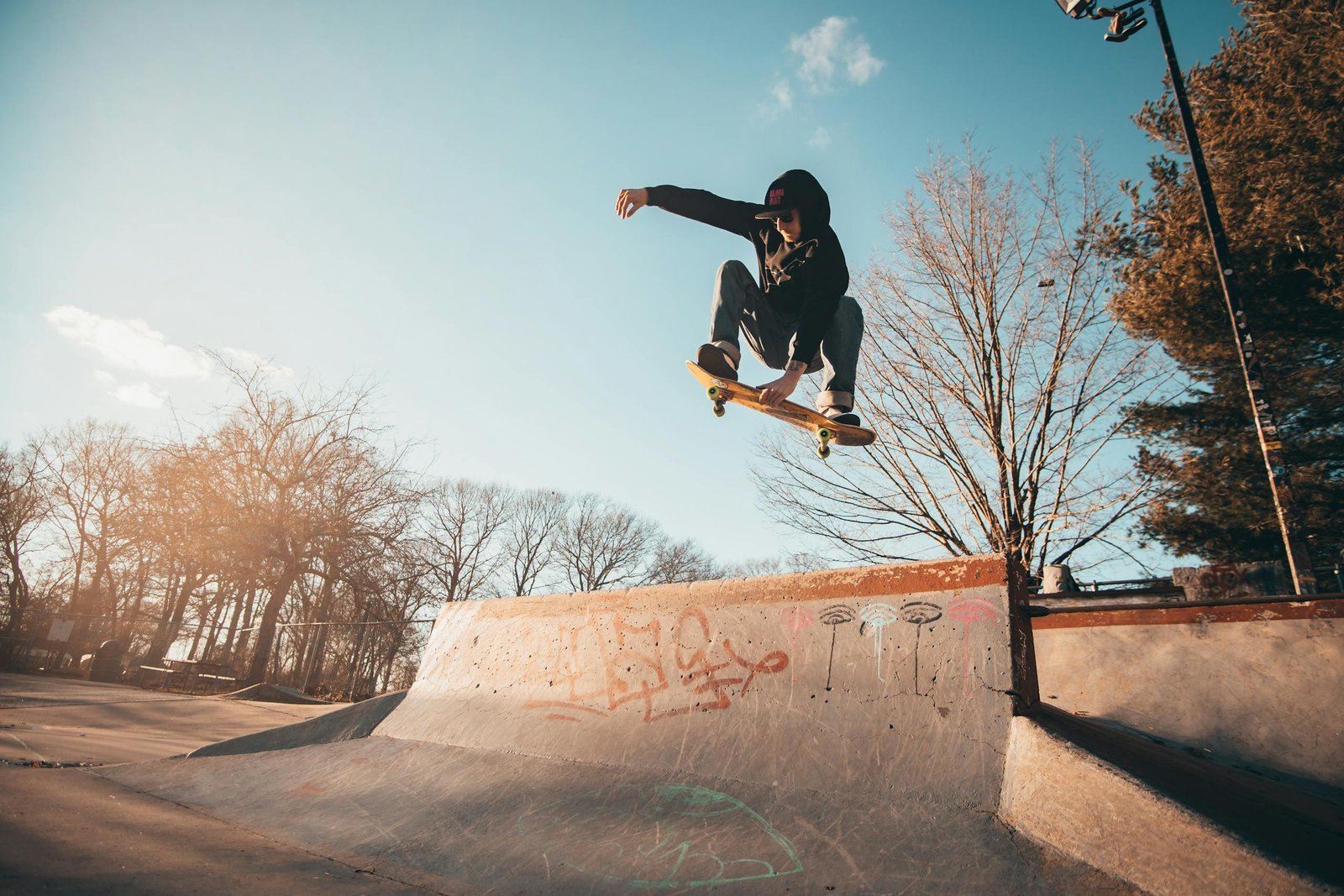 A skateboarder performs an aerial trick at a skate park on a sunny day, displaying skill and agility.