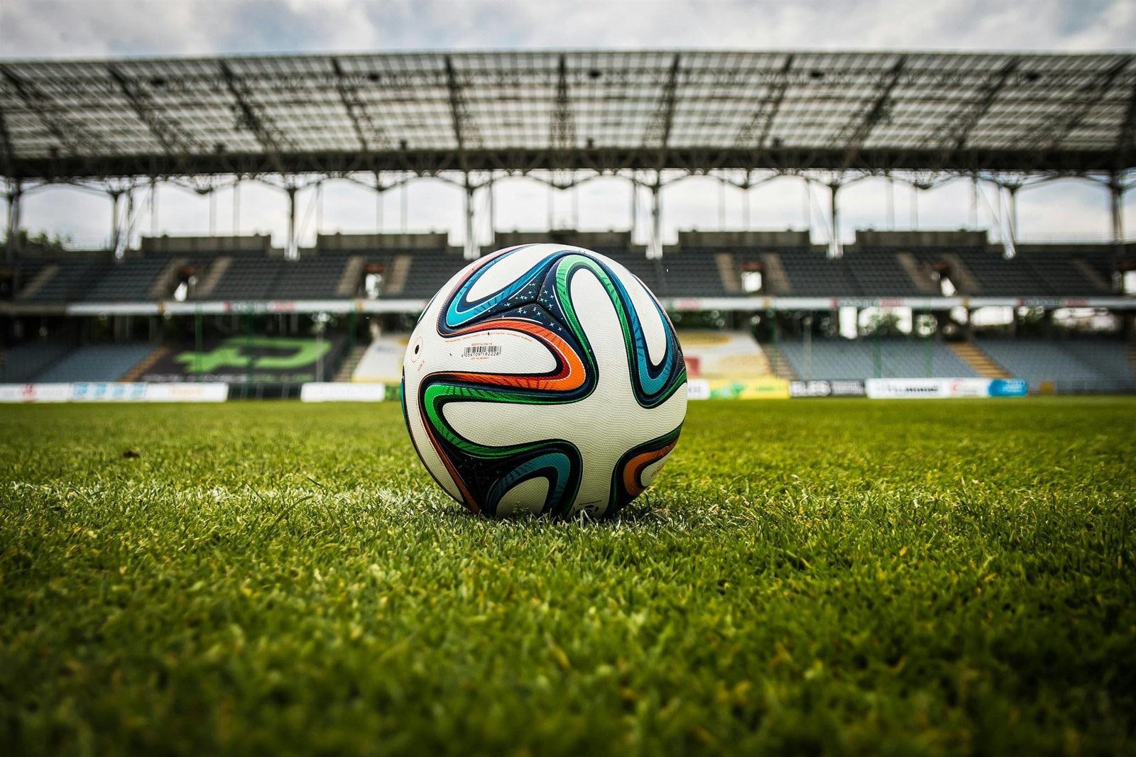 A vibrant soccer ball rests on a lush green field inside an empty stadium, capturing the essence of sports.