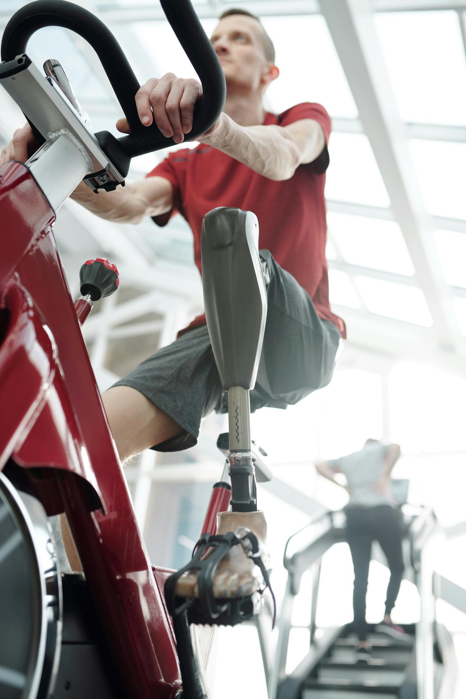 An adult man with a prosthetic leg exercises indoors on a stationary bike, focusing on fitness and resilience.