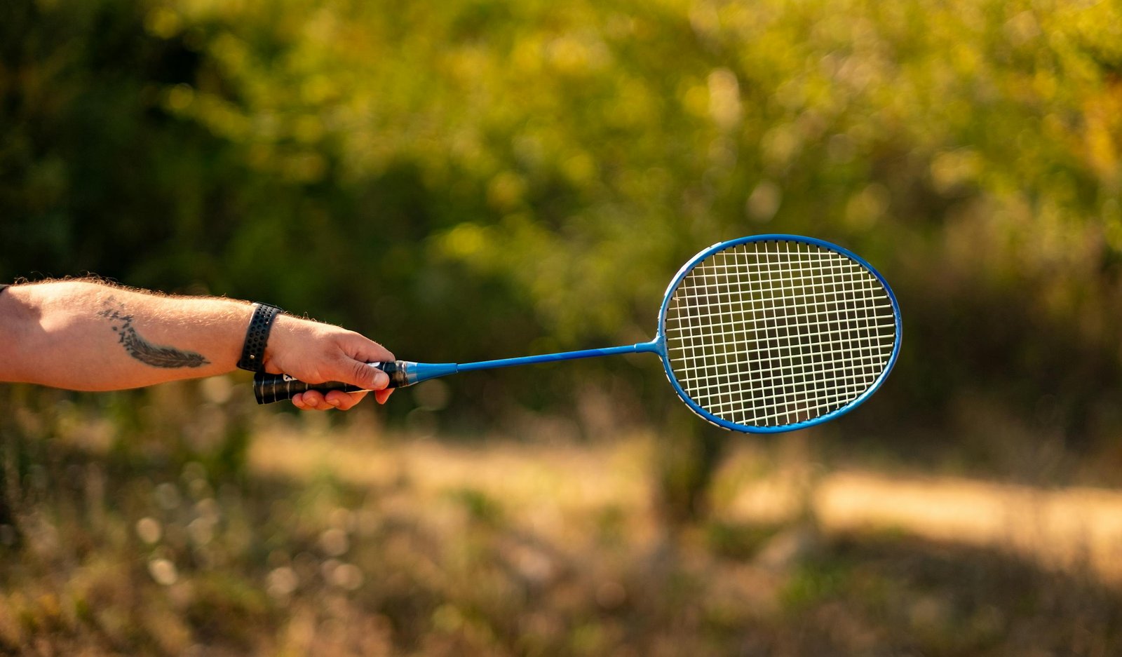 Close-up of a hand holding a blue badminton racket outdoors, perfect for summer sports vibe.