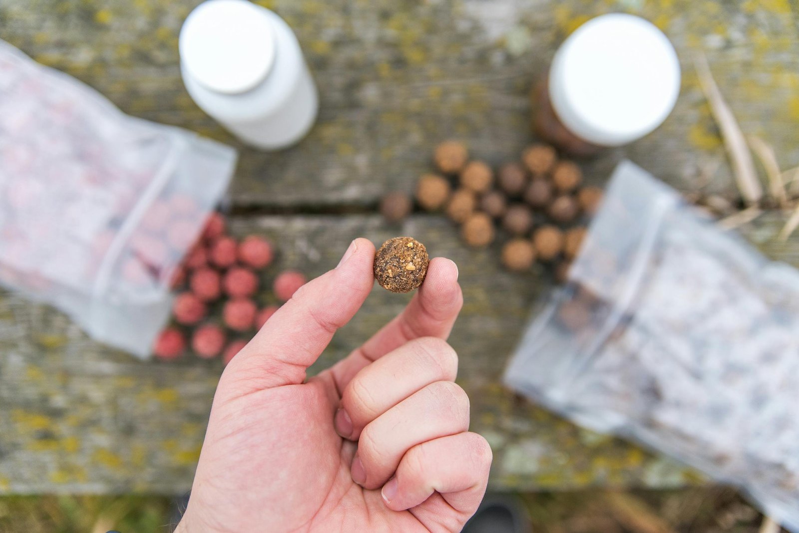 Close-up of a hand holding a fishing bait with supplies on a wooden table.