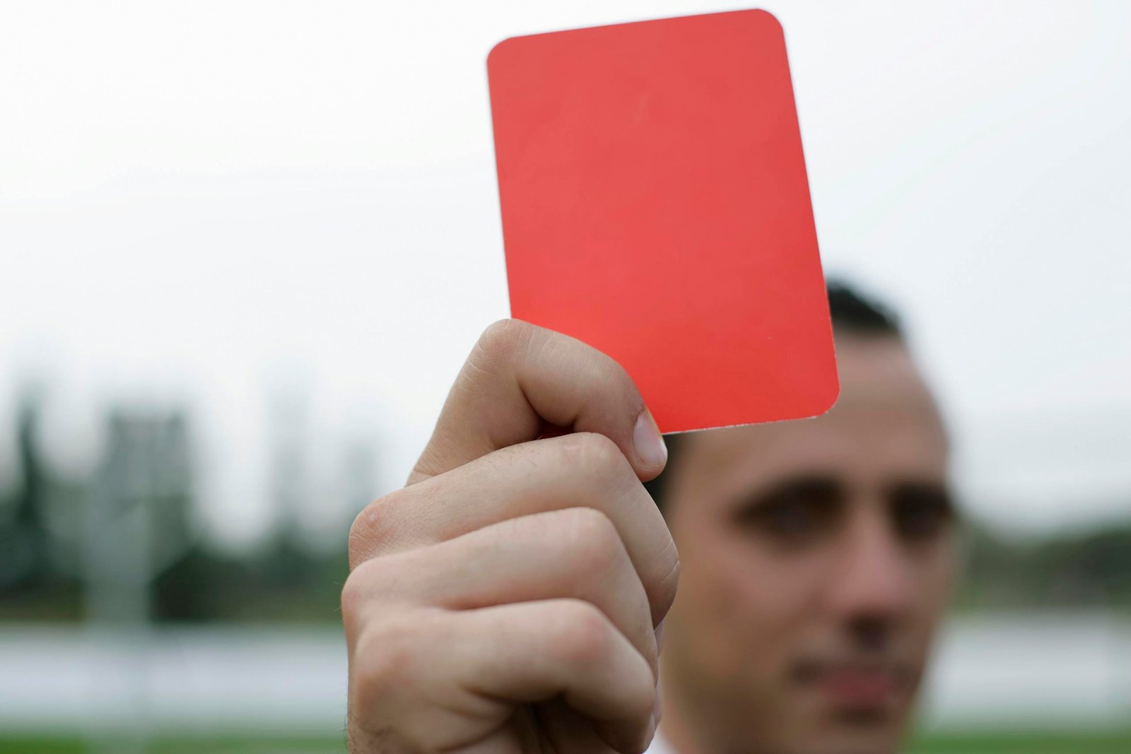 Close-up of a referee holding a red card, signaling a penalty in a soccer match.