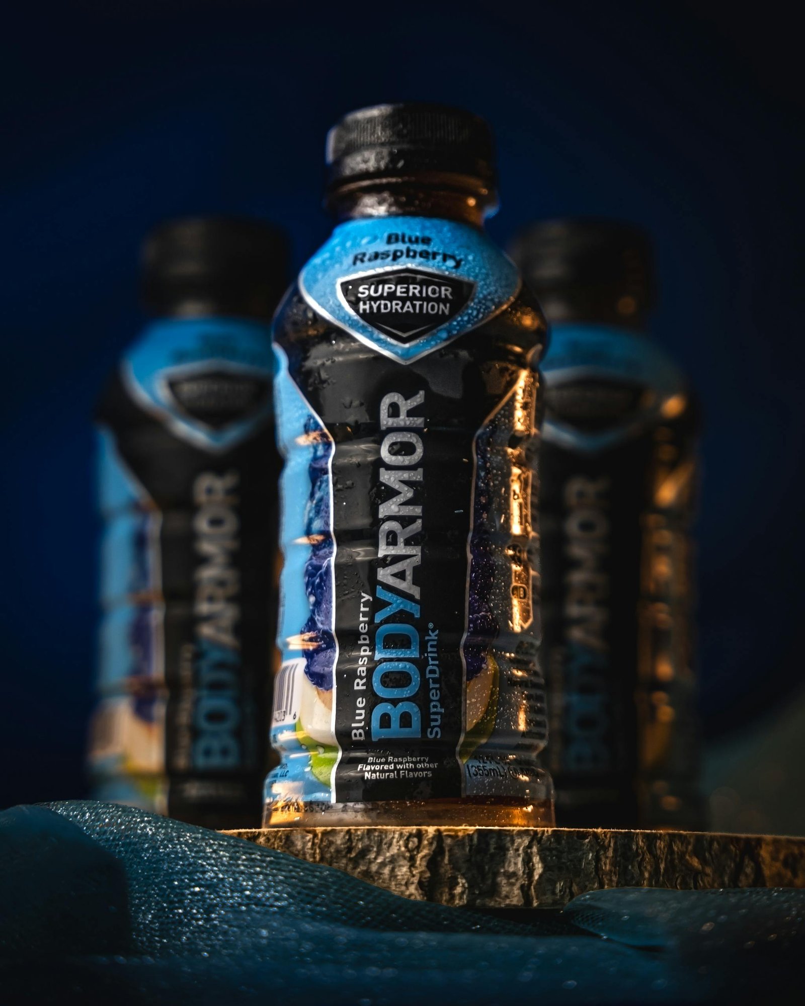 Close-up of blue raspberry sports drink bottles with focus on front bottle highlighting texture and label.