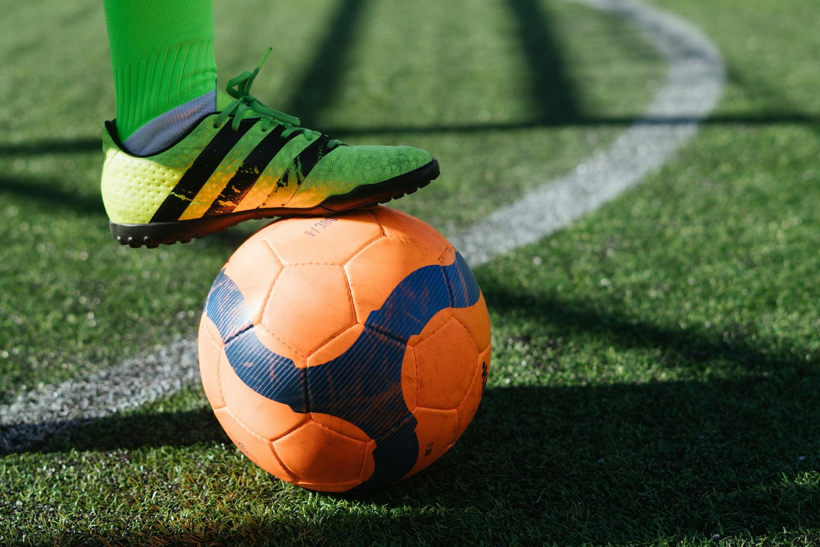 Dynamic shot of a soccer player's foot on a vivid orange ball on a lush green field.