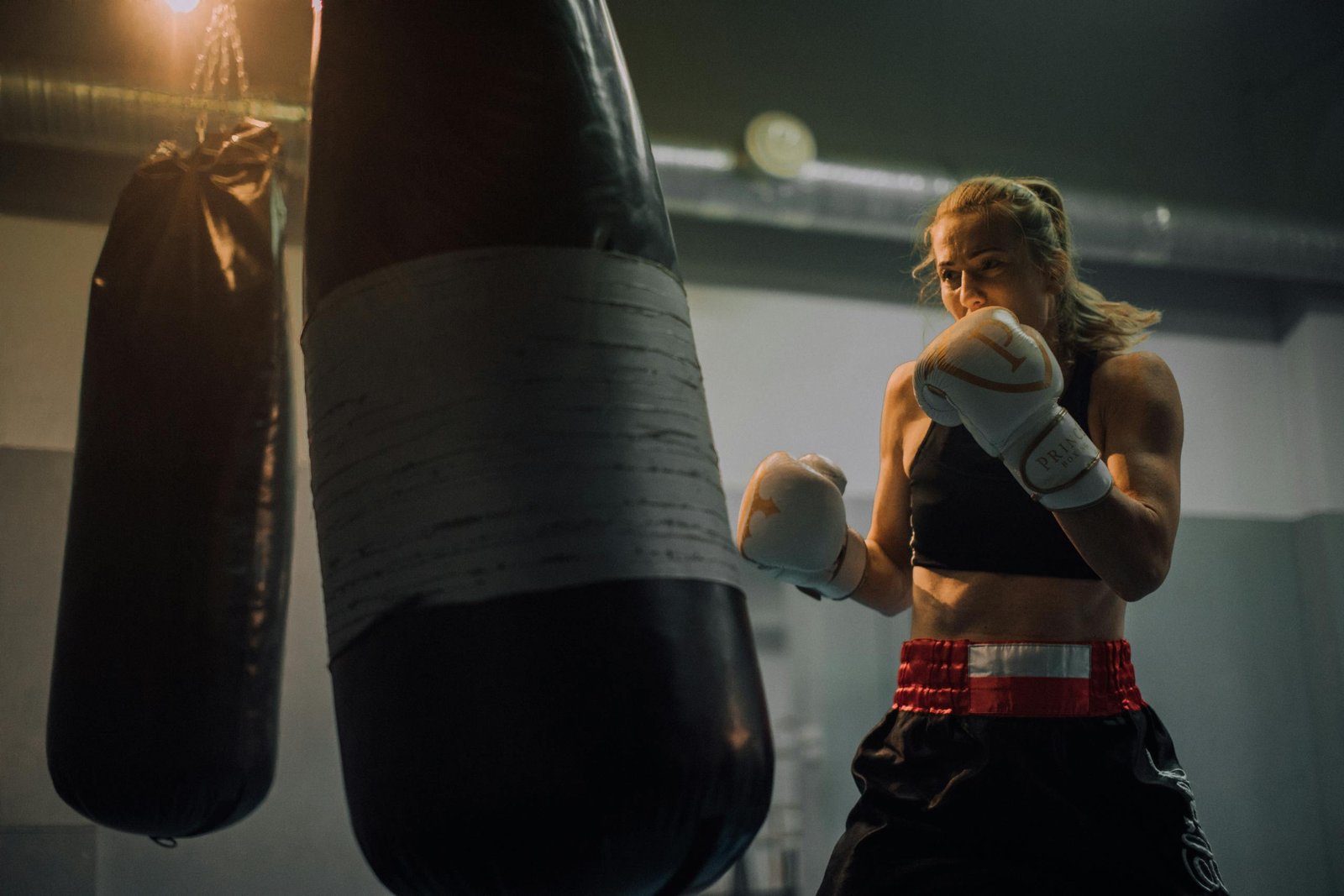 Fierce female boxer honing her skills in a gym, delivering powerful punches to a heavy bag.