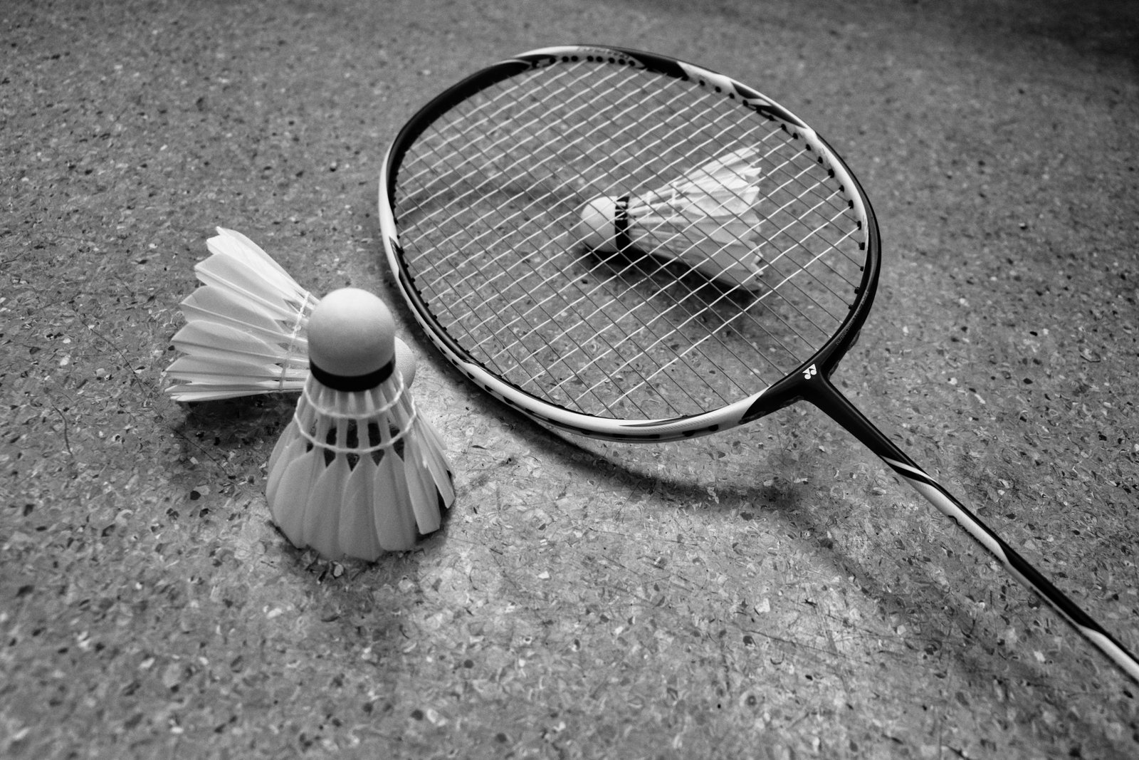 Grayscale image of badminton racket and shuttlecocks on a court surface.