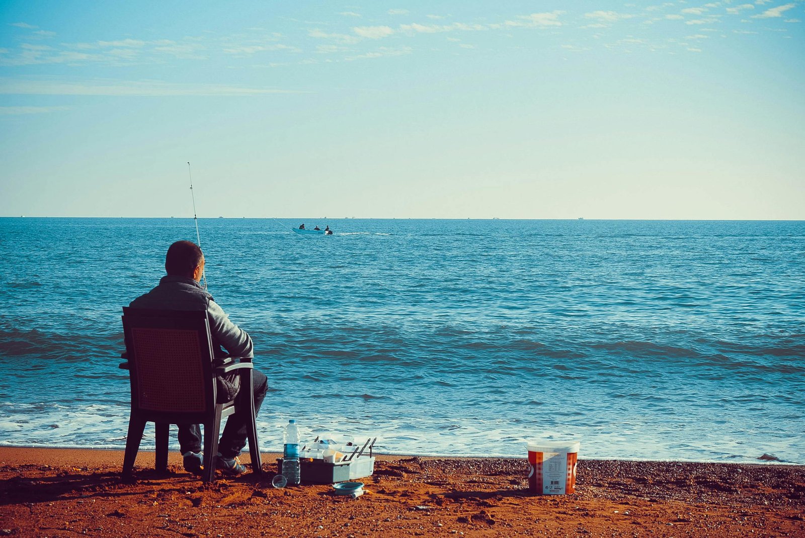 Man fishing on Antalya's tranquil beach with clear blue waters and sandy shore.