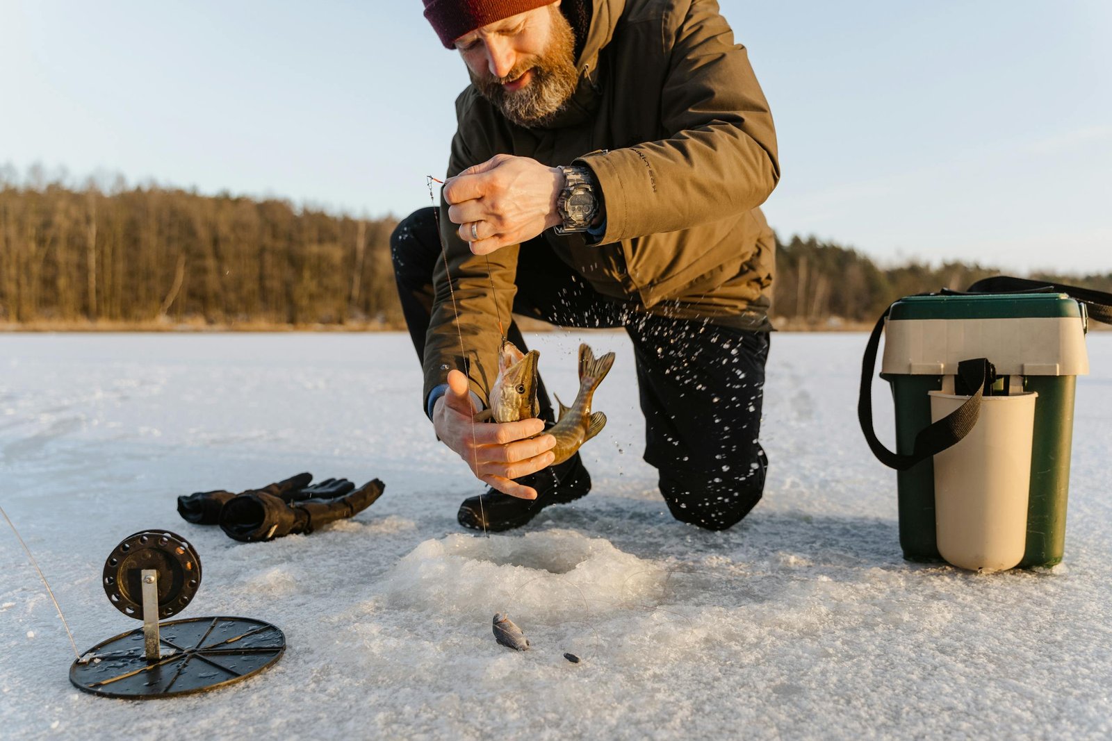 Man ice fishing on a frozen lake during winter, catching fish through a hole in the ice.