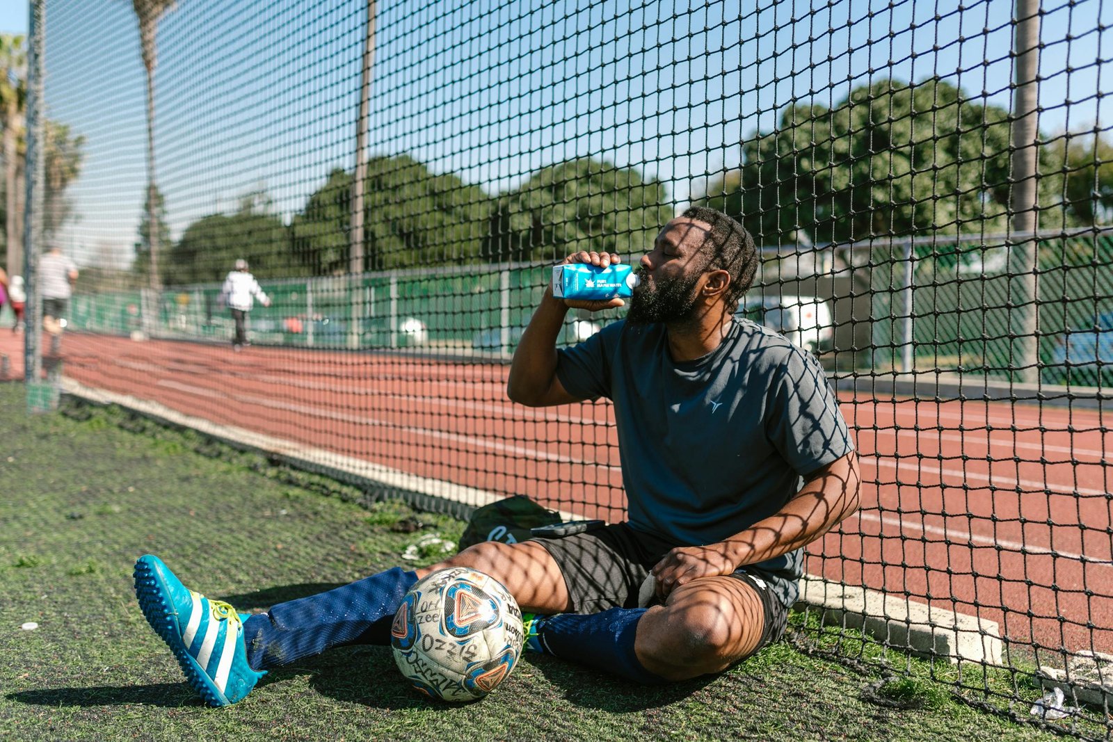 Soccer player resting by a field, hydrating after practice on a sunny day.