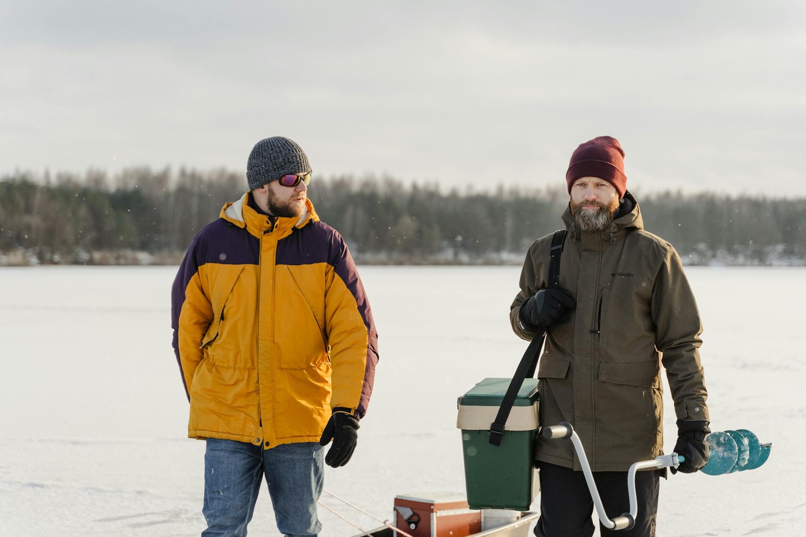 Two men enjoying ice fishing on a frozen lake, equipped with gear.