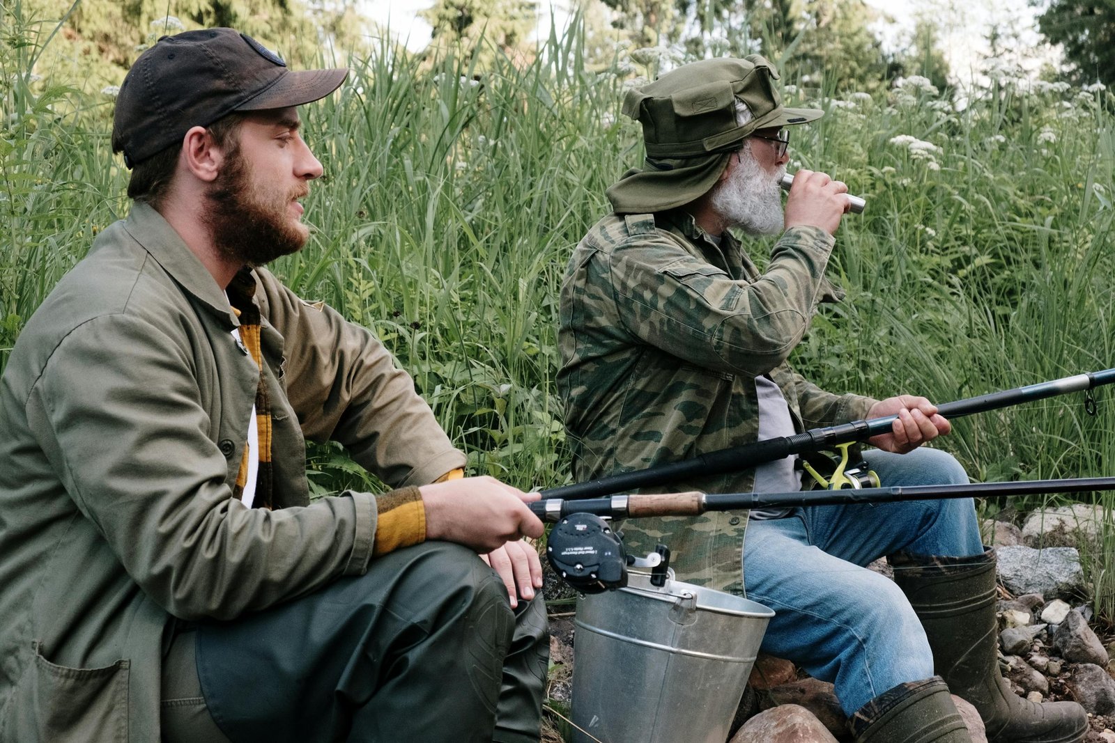 Two men fishing and enjoying nature near a lush green lakeside.