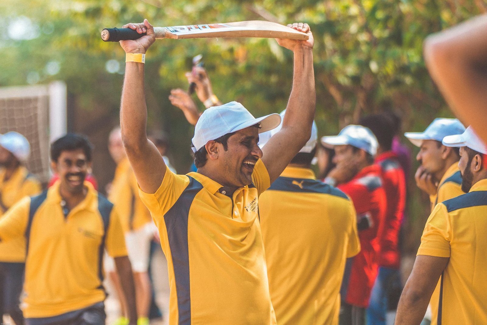 A cricketer in yellow uniform celebrating with a cricket bat raised in triumph outdoors.