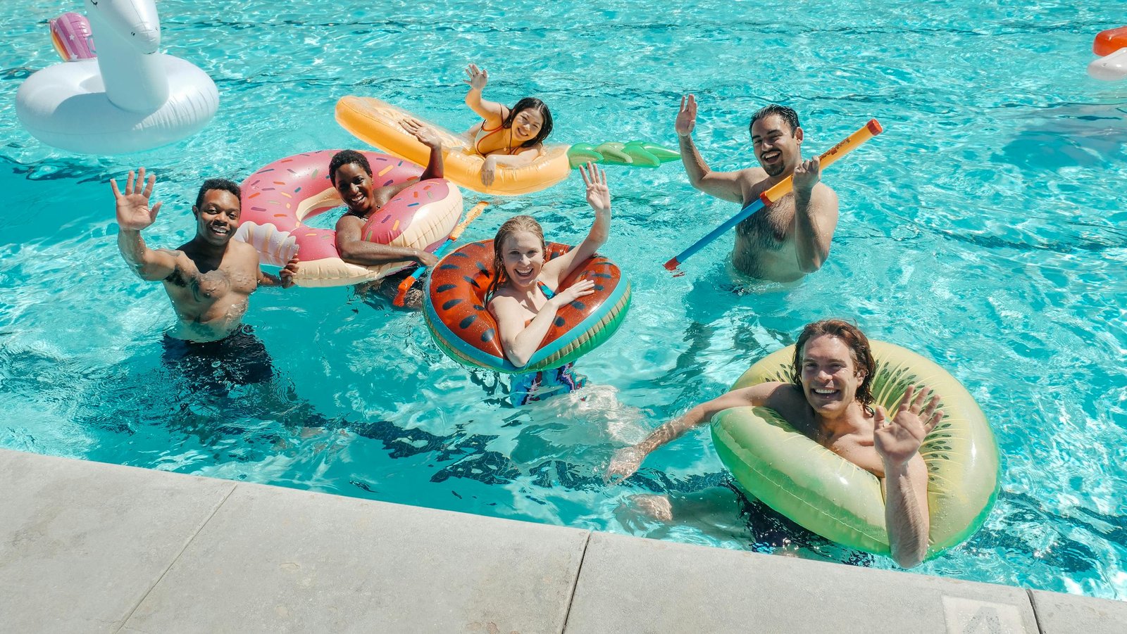 A diverse group of friends waving and having fun at a lively summer pool party.