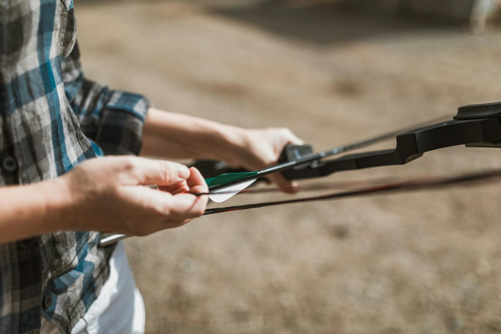 A person prepares a recurve bow with arrows outdoors, ideal for archery enthusiasts.