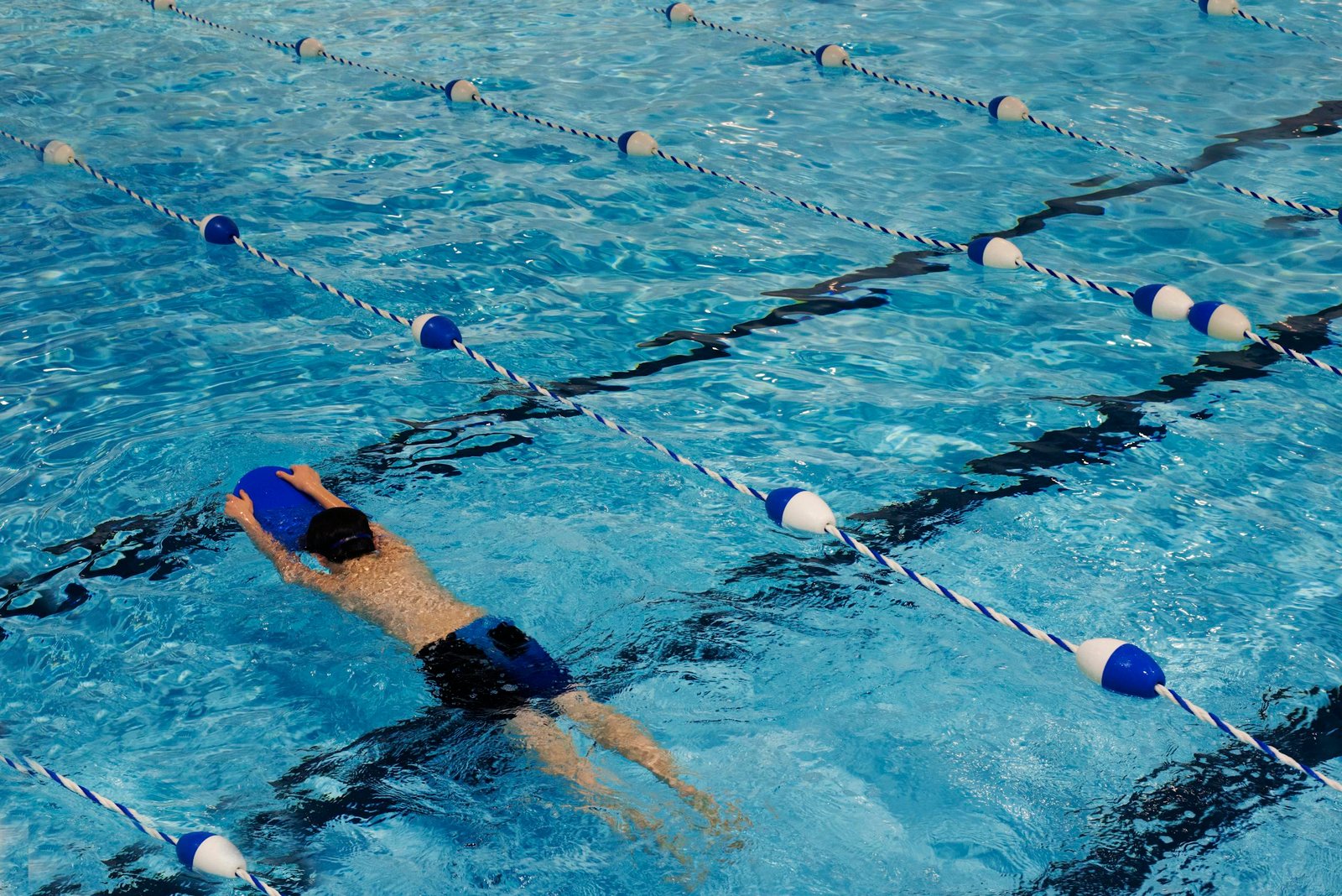 A young swimmer practicing with a kickboard in a swimming pool on a sunny day.