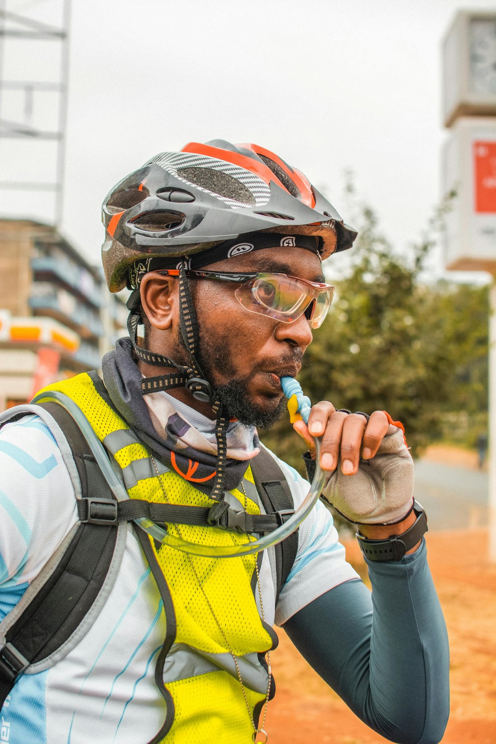 Adult male cyclist in helmet using hydration pack outdoors, showcasing active lifestyle.