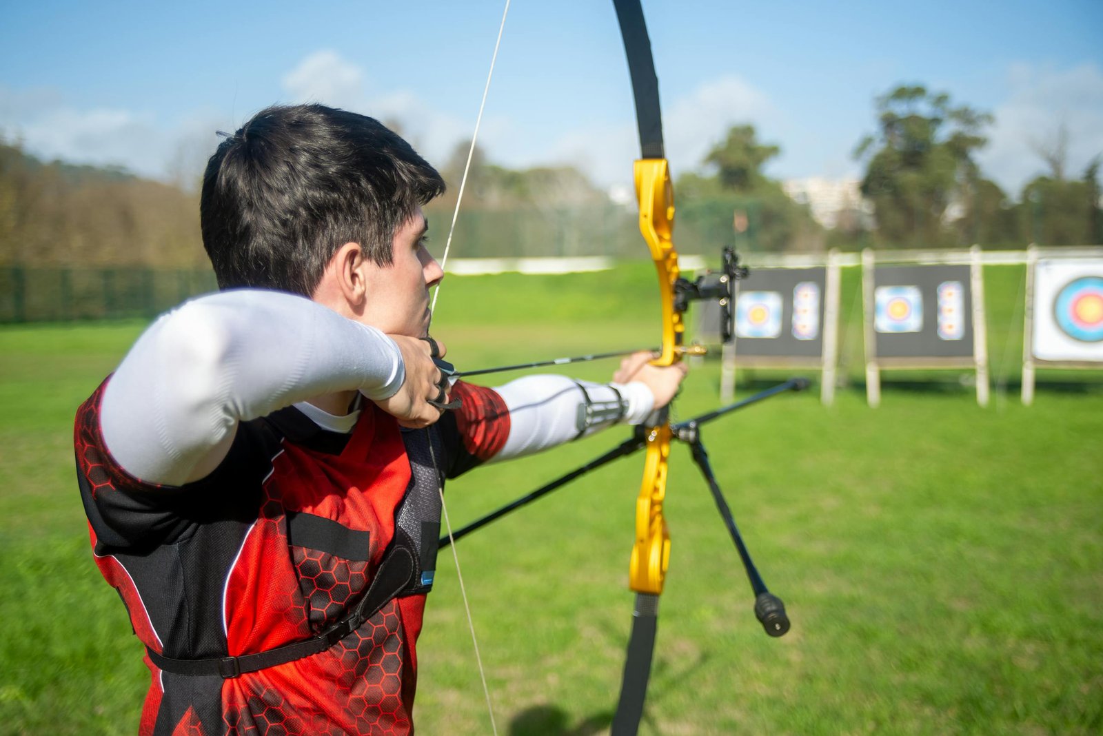 An archer aiming a bow at targets in an outdoor field on a sunny day.