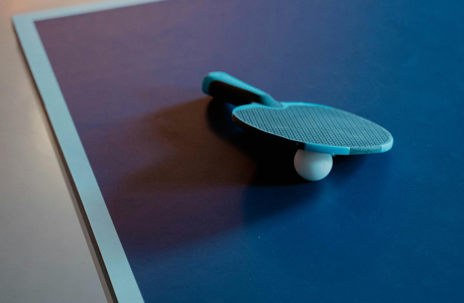 Close-up of a table tennis paddle and ball on a blue table, indoor setting.