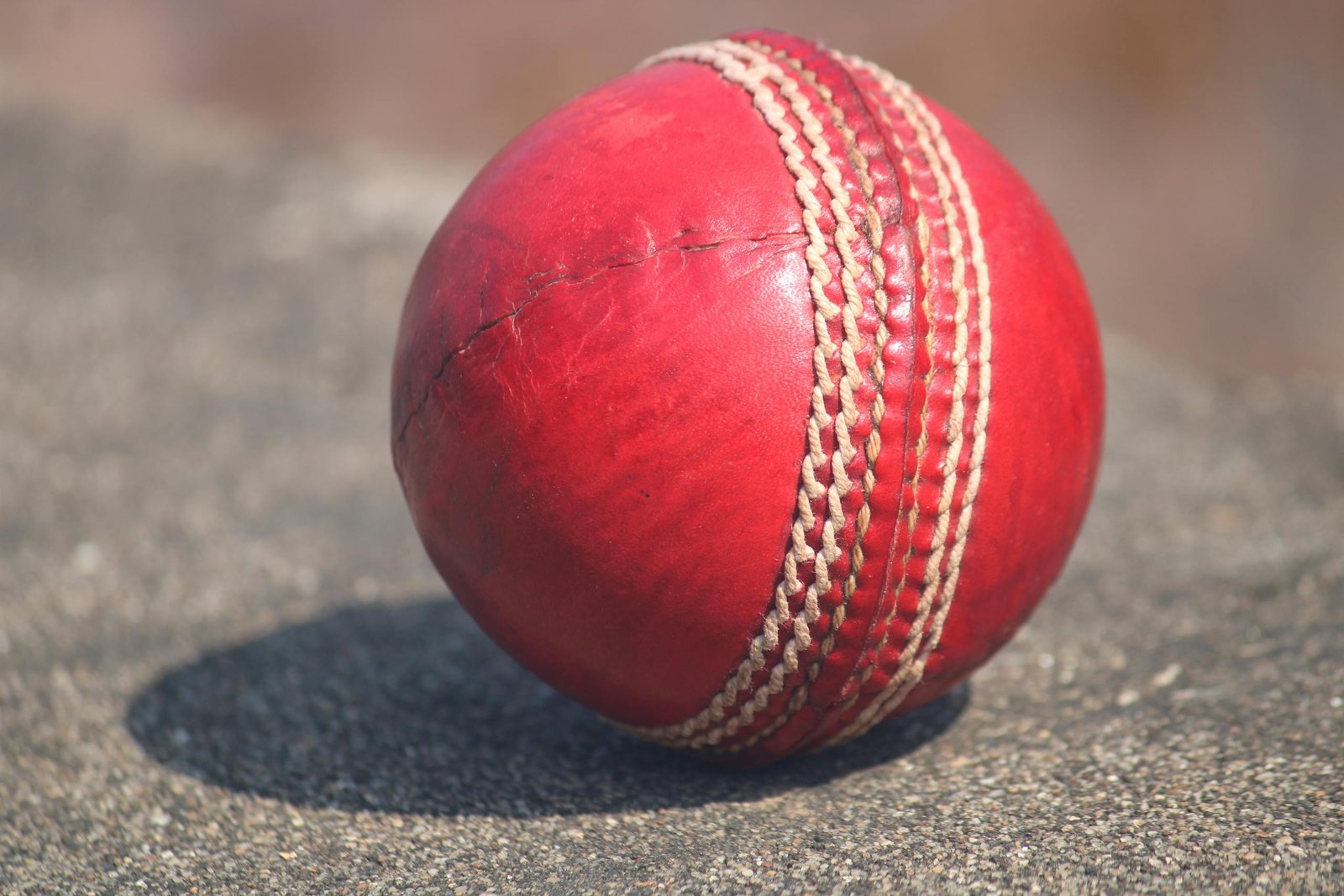 Detailed view of a textured red cricket ball outdoors in sunlight.