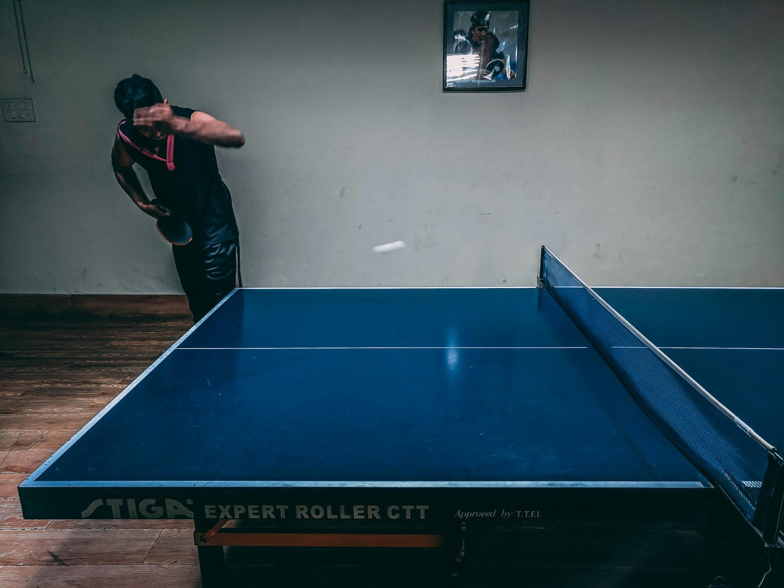 Dynamic action shot of a man playing table tennis indoors, capturing a moment of intense focus and skill.