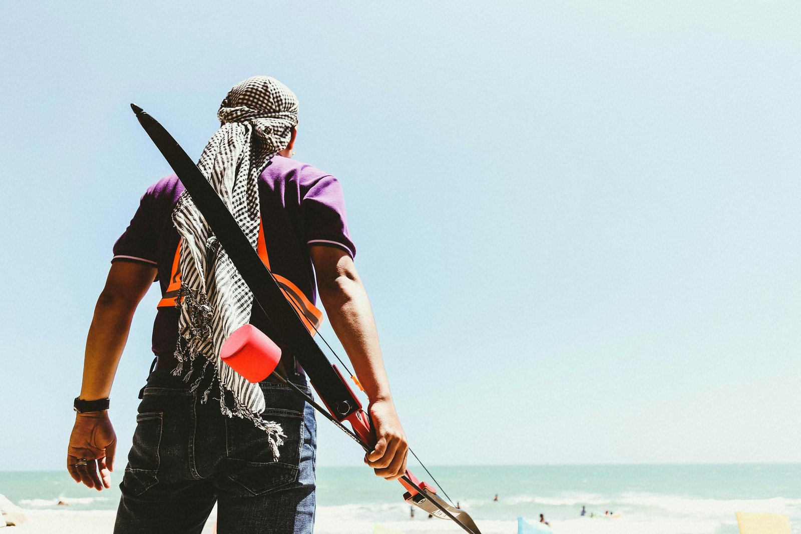 Person standing on a beach with a bow, enjoying a bright summer day by the ocean.