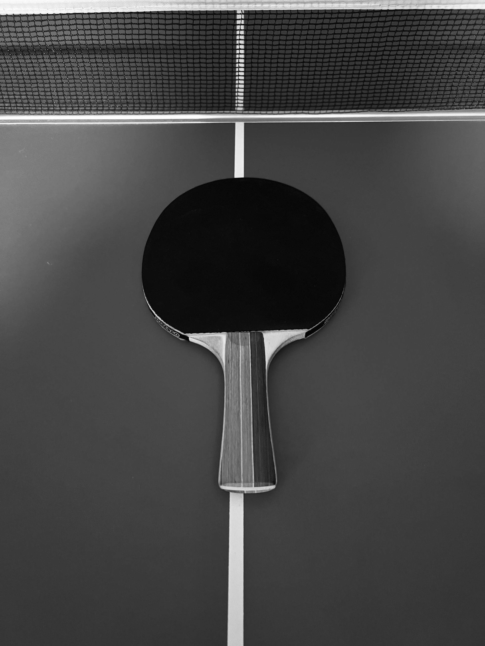 Table tennis paddle placed on a ping pong table in striking black and white contrast.