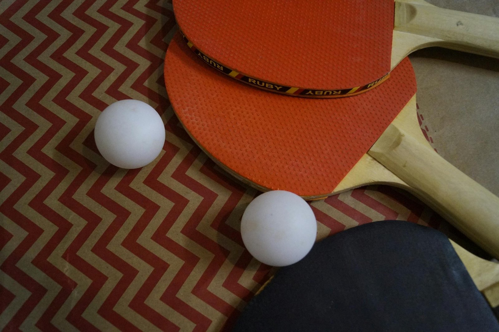 Table tennis paddles and balls arranged on a zigzag patterned surface, showcasing sports equipment essentials.