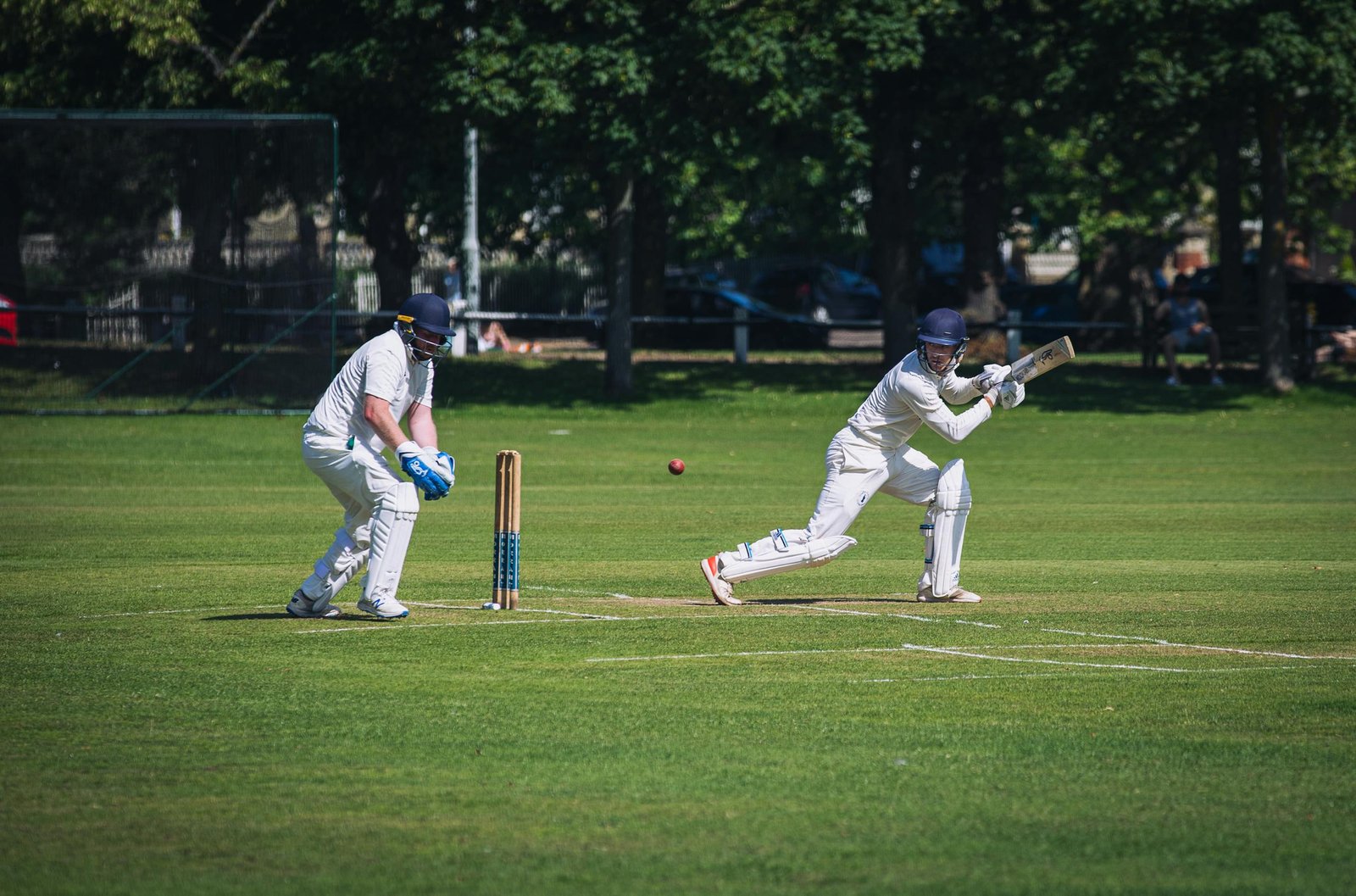 Two cricket players in action during a sunny match on a lush green field in London.