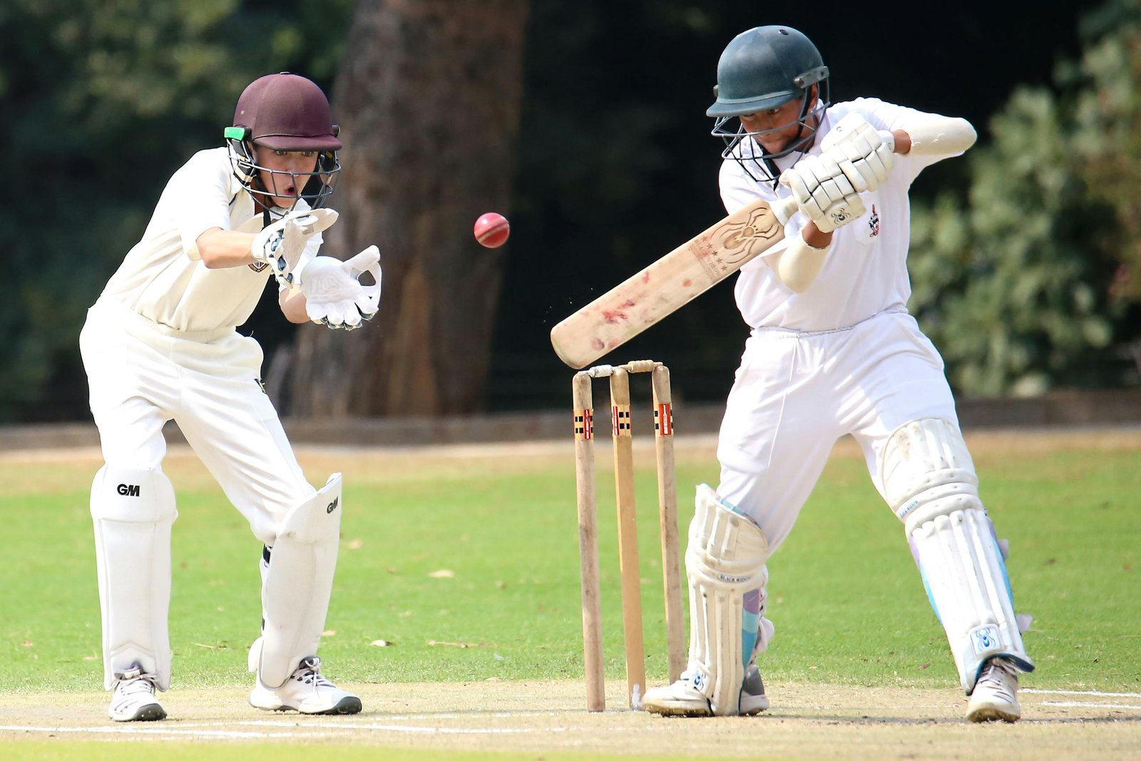 Two cricket players in action on a sunny day, showcasing skillful batting and wicket-keeping.