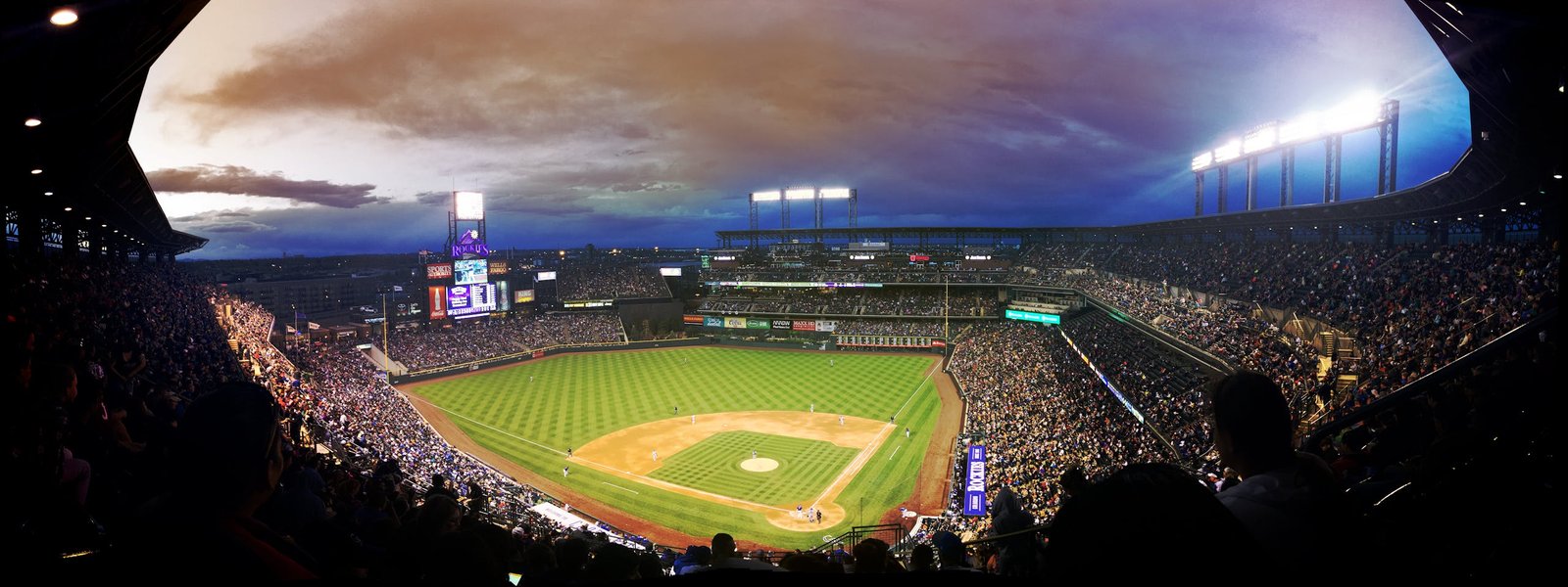 Wide-angle view of a baseball stadium at dusk capturing the field and excited crowd.